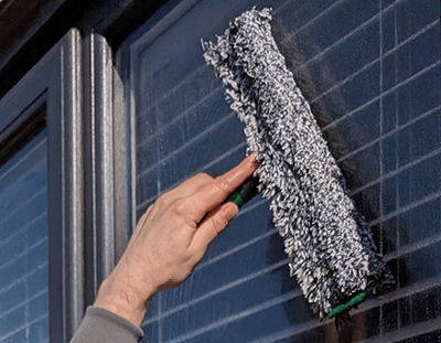 Technician performing residential window cleaning with squeegee in South Elmsall.
